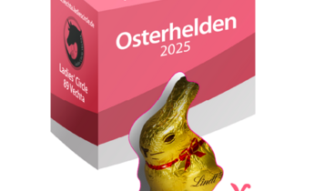 Die Verpackung der Schokohasen der Osterhelden Aktion. Der obere Teil ist pink. Der untere weiß. Am unteren Rand sind pinke Silhouetten von Osterhasen und Ostereiern zu sehen. In der Mitte der Verpackung ist ein Sichtfenster in dem der Lindt-Schokoladenhase zu sehen ist. 