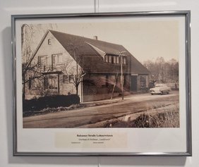 Eine schwarz-weiß Fotografie des alten Hauses das damals die Gaststätte kl. Holthaus "Laubfrosch" beherbergt hat. Vor dem Haus stehen noch ein alter Auto und ein Fahrrad. 