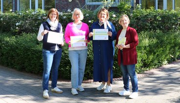 Die Organisatorinnen stehen an der Rückseite des Ludgerus-Werk zusammen. Sie halten das Schild des Bücherflohmarkts in den Händen. Es ist ein sonniger Frühlingstag. 