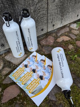 Die Preise für das Stadtquiz vom Stadtfest Lohne. Zwei Flaschen mit dem Logo des Ludgerus-Werks stehen im Hintergrund. Eine gleiche Flasche liegt am rechten Rand. Davor liegen drei Gutscheine des Ludgerus-Werks. 