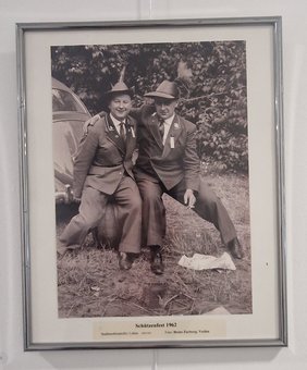 Eine schwarz-weiß Fotografie von zwei Schützen in Anzügen. Sie sitzen zusammen auf einem Fass und umarmen sich. Sie posieren für die Fotografie.