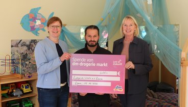 Drei Personen stehen vor eine Spielecke. Sie halten einen Scheck in Höhe von 600 € in den Händen.