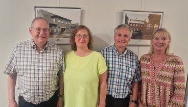 Eine Gruppe von vier Leuten. Sie stehen vor einer weißen Wand. An der Wand hängen schwarz-weiß Bilder von alten Gaststätten in Lohne. 