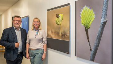 Fotograf Willi Rolfes und Leiterin Annette Kröger posieren für ein Bild. Sie stehen vor ein paar Fotografien von Willi Rolfes Baumaufnahmen.