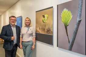 Fotograf Willi Rolfes und Leiterin Annette Kröger posieren für ein Bild. Sie stehen vor ein paar Fotografien von Willi Rolfes Baumaufnahmen.
