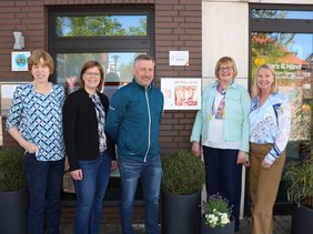 Eine Gruppe Menschen stehen vor einem Außern-Defibrillator und schauen in die Kamera.