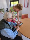 Mitarbeiterin zeigt einem Senior die Bedienung eines Tablets