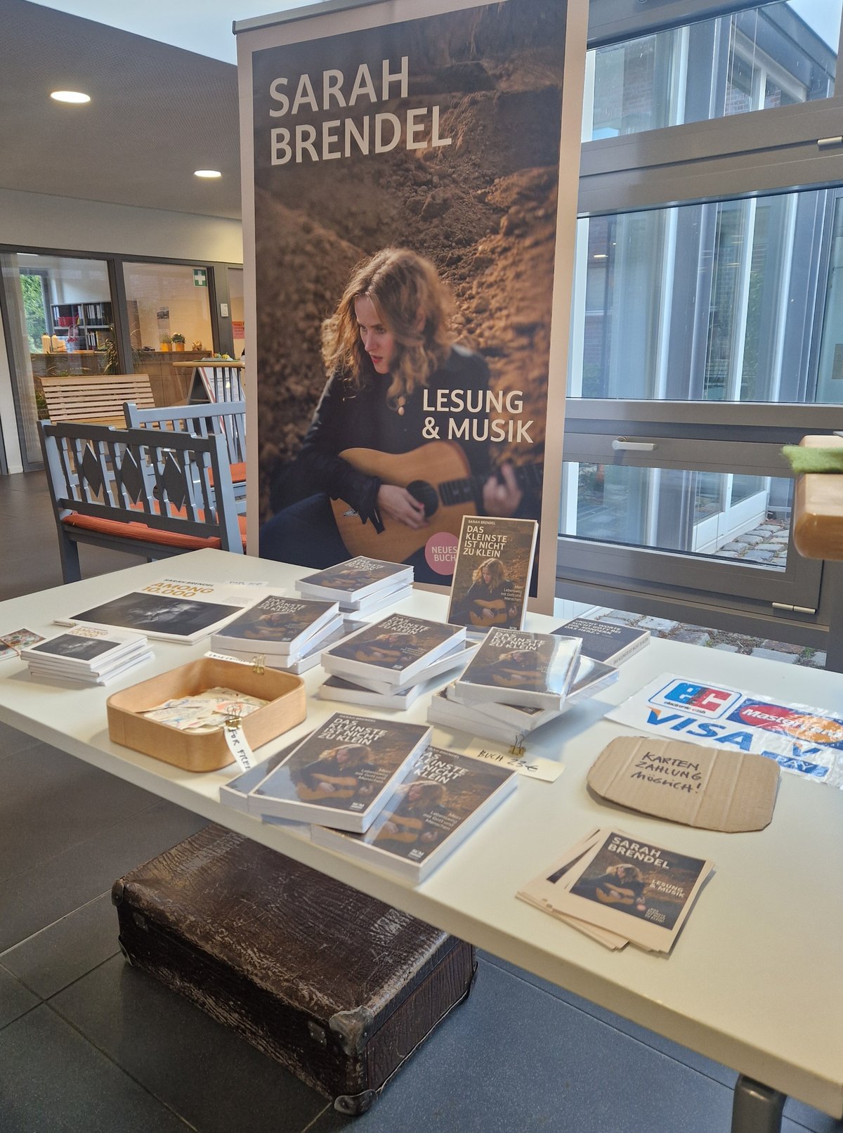 Ein mit Bücher und Merchandise bestückter Tisch mit einem Roll-Up dahinter.