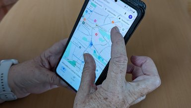 Ein Smartphone das von einer Hand bedient wird. Die Hand gehöert zu einer älteren Person.