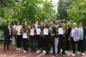 Die Gruppe von Teilnehmenden stehen zusammen mit den Lehrerinnen vor einer Reihe Büsche. Sie halten ihre Abschlusszeugnisse und eine Sonnenblume in den Händen