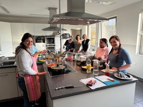 Eine Gruppe Frauen stehen um eine Kochinsel herum und bereiten leckeres Essen zu. 