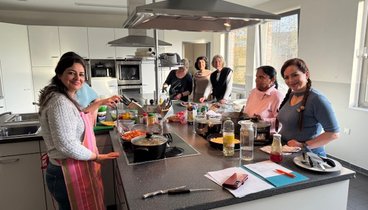 Eine Gruppe Frauen stehen um eine Kochinsel herum und bereiten leckeres Essen zu. 