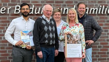 Eine Gruppe von 5 Leuten stehen vor dem Logo an der Außenwand des Ludgerus-Werk e.V. Lohne. Annette Kröger, die zweite Person von rechts, hält ein Plakat für den Vortrag "Haltung zeigen" von Marlies Stertenbrink in den Händen. 