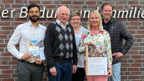 Eine Gruppe von 5 Leuten stehen vor dem Logo an der Außenwand des Ludgerus-Werk e.V. Lohne. Annette Kröger, die zweite Person von rechts, hält ein Plakat für den Vortrag "Haltung zeigen" von Marlies Stertenbrink in den Händen. 