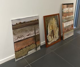 Drei Bilder der Künstlerinnen lehnen an einer Wand bereit zum Aufhängen. 