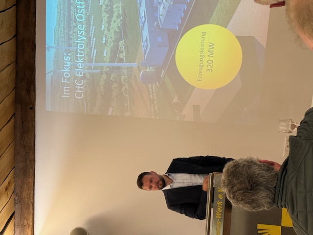 Der Dozent am Rednerpult. Im Hintergrund sieht man die Präsentation des Vortrags auf einer Leinwand.